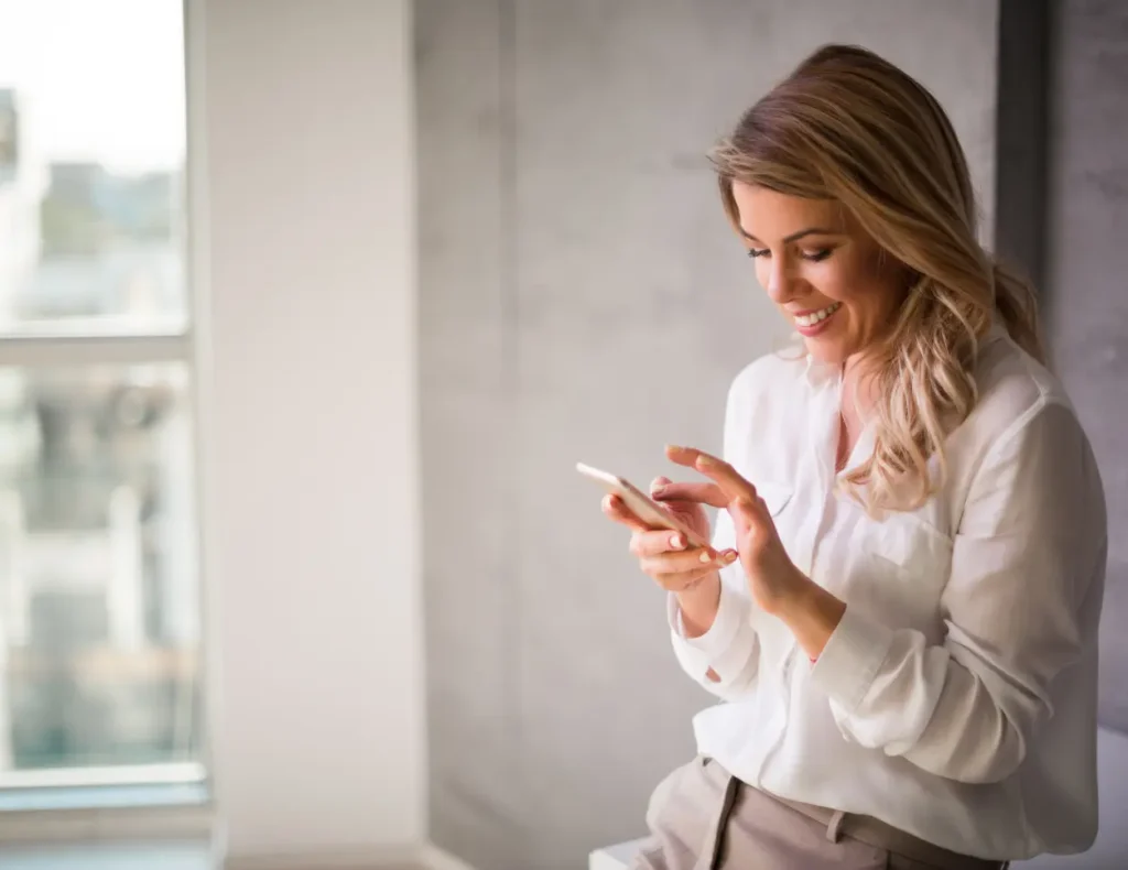 Lächelnde Frau, die sitzend mit ihrem Smartphone interagiert, für den Social-Media-Service der Digital Agency Jinni S.r.l.