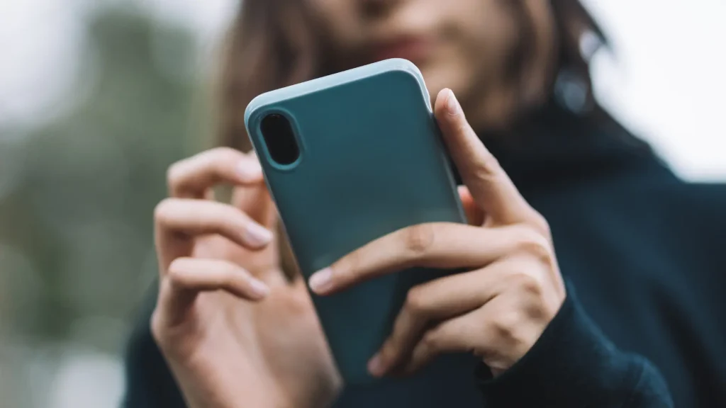 Junge Frau mit Smartphone in der Hand vor unscharfem Hintergrund zum Thema häufige Fehler im Social-Media-Management