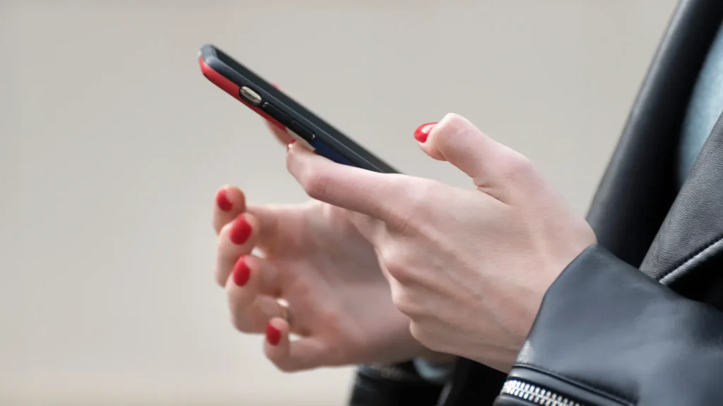 Hand einer Frau mit rotem Nagellack, die ein Smartphone benutzt, zum Thema häufige Fehler im Social-Media-Management