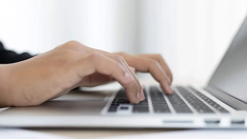 Mains tapant sur le clavier d'un ordinateur portable pour identifier les raisons d'avoir un site web en 2025