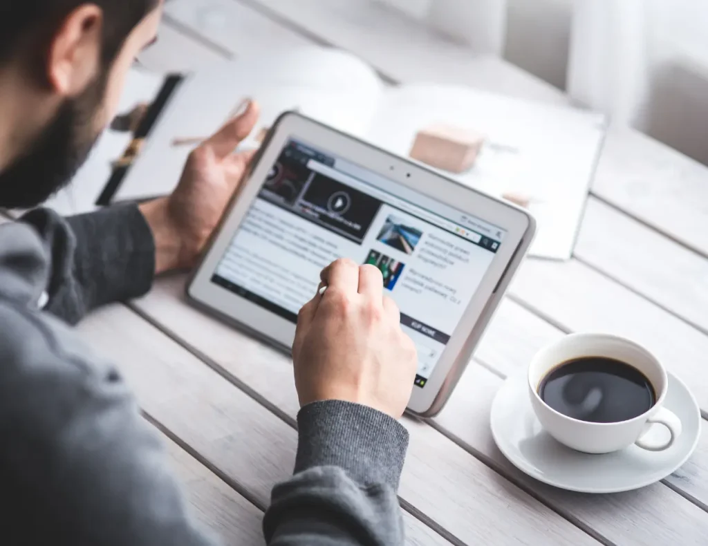 Mann ruft auf einem Tablet eine Website auf, mit einer Tasse Kaffee auf dem Tisch, für den Service der Digital Agency Jinni S.r.l.
