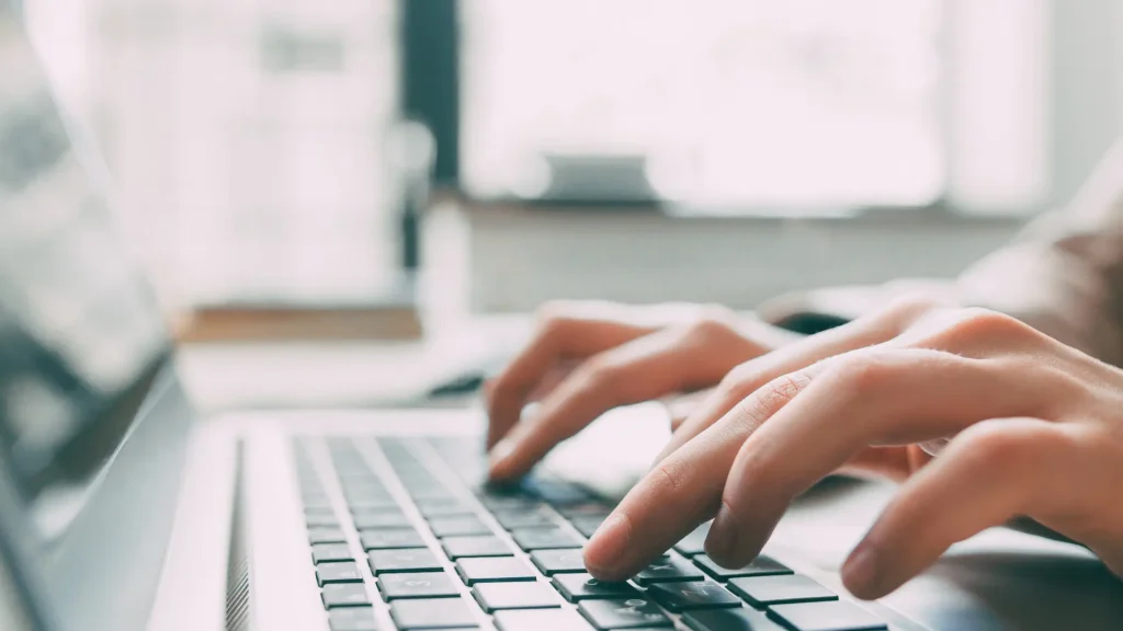 Hände, die auf der Tastatur eines Laptops tippen, mit natürlichem Licht im Hintergrund, für den Artikel über die Verbesserung des Website-Rankings