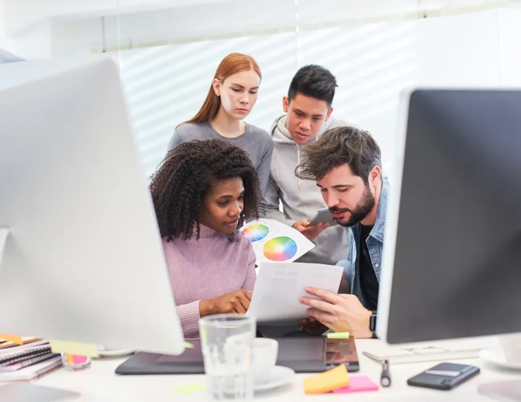 Multiethnisches Kreativteam arbeitet gemeinsam an Farbpaletten vor Computern.