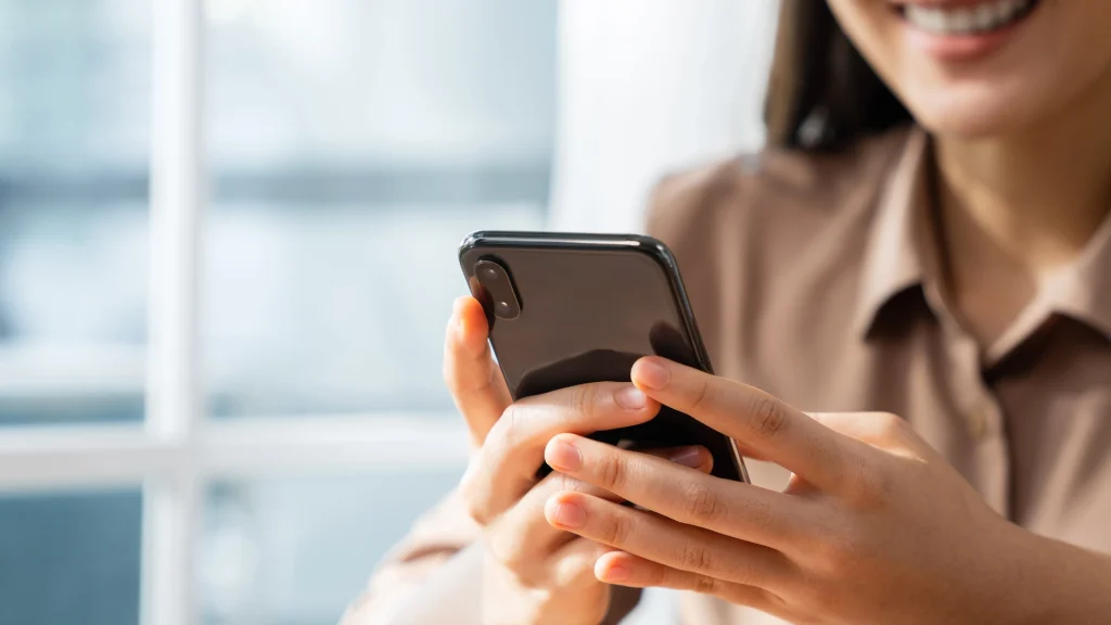 Primer plano de una mano que sostiene un smartphone, con una sonrisa visible en el rostro de la persona, para el artículo sobre formatos de redes sociales