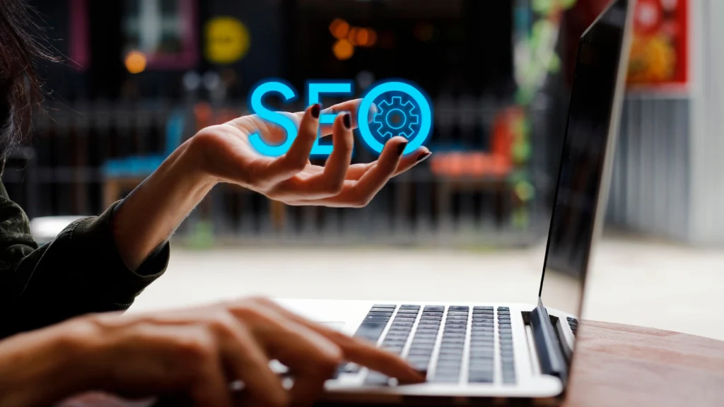 Mano sosteniendo el rótulo luminoso “SEO” sobre un portátil, símbolo de la visibilidad en los motores de búsqueda