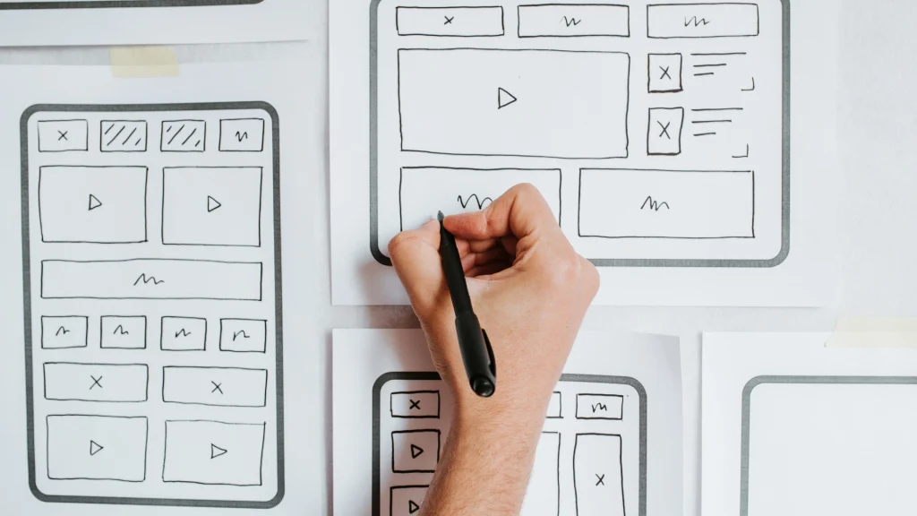 Person zeichnet von Hand Wireframes einer Startseite auf Papierbögen – UX-Design und Struktur einer Website.
