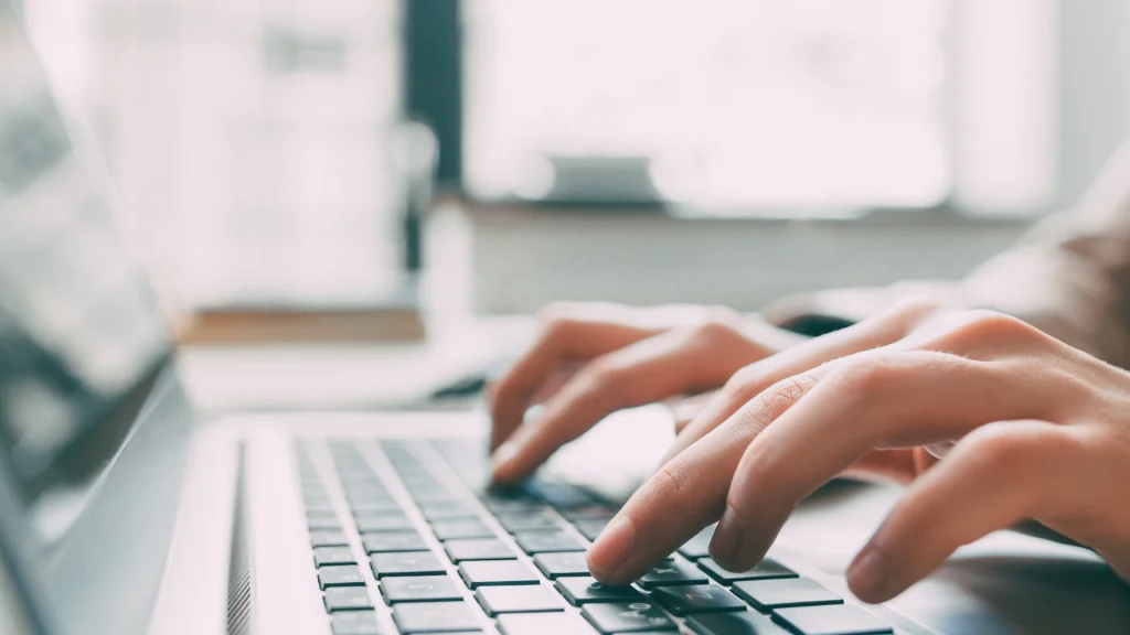 Hands typing on a laptop keyboard in bright environment, symbol of SEO effectiveness measurement work