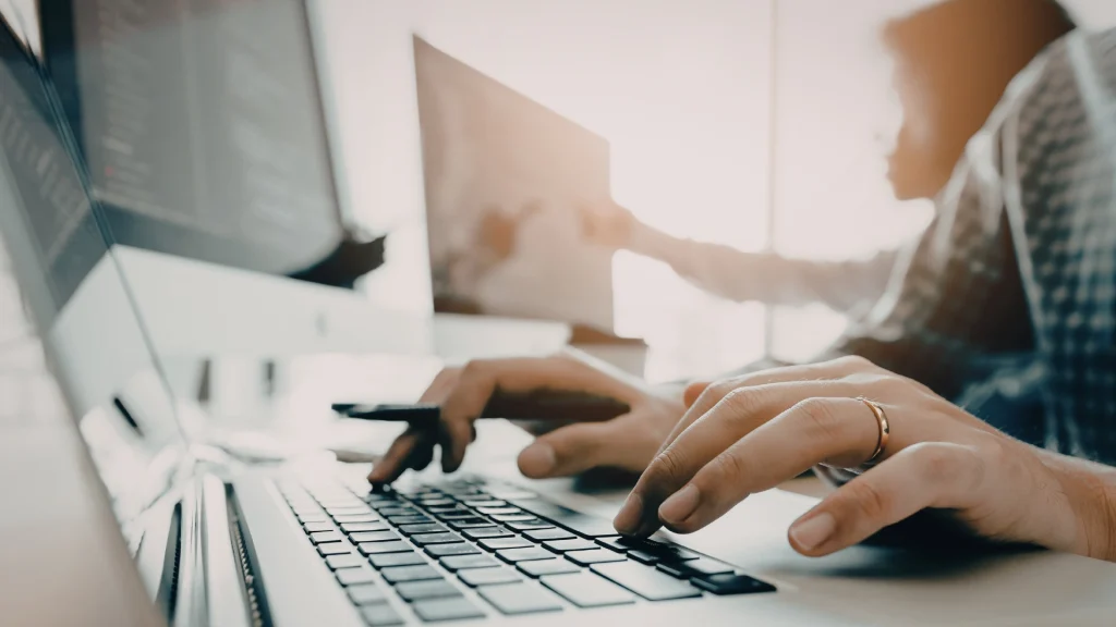 Pessoa a trabalhar ao computador com as mãos no teclado num contexto digital