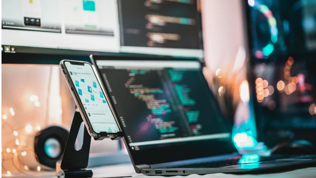 Smartphone auf einem Ständer vor einem Laptop mit Programmiercode