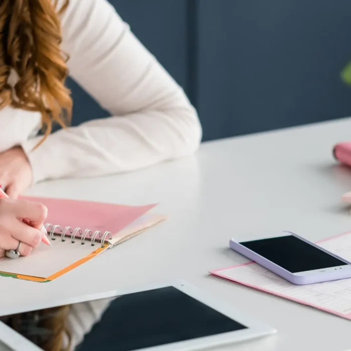 Donna che scrive su un quaderno con planner e dispositivi digitali sul tavolo per la guida sulle principali tipologie di contenuti per i social media.