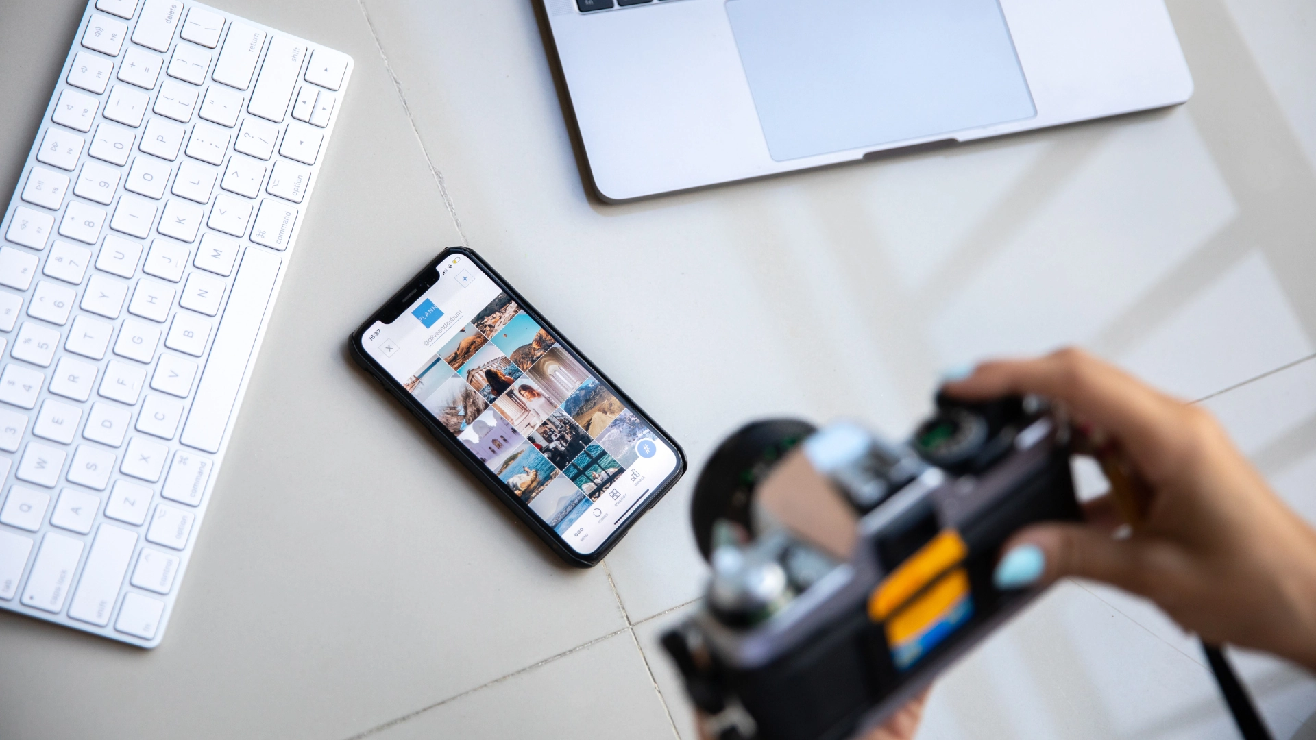 Smartphone resting on a desk showing a grid gallery of images, flanked by a keyboard and camera for the article on social media formats