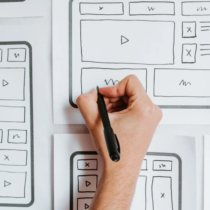 Persona che disegna a mano wireframe della homepage su fogli di carta, concetto di progettazione UX e struttura sito web.