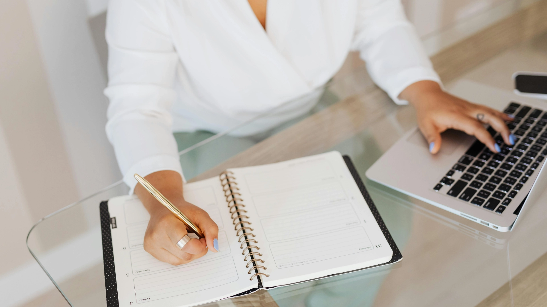 Persona che scrive su agenda mentre lavora al computer portatile